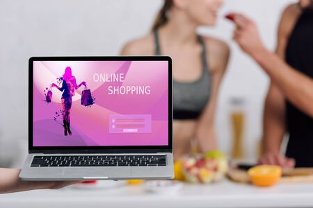 selective focus of laptop with online shopping website on screen near couple in kitchen