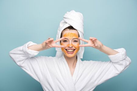 cheerful girl with citrus facial mask showing victory gestures on blue backgroundの写真素材