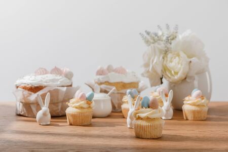 Selective focus of cupcakes with decorative bunnies, sugar bowl, easter cakes and vase with flowers isolated on greyの写真素材
