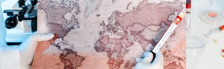 panoramic shot of scientist holding sample with coronavirus lettering near map