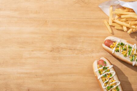top view of delicious hot dogs with corn, green onion and mayonnaise near french fries on wooden tableの写真素材