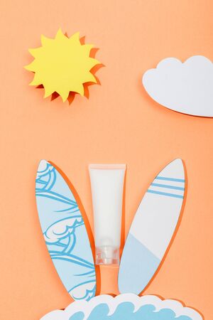 Top view of paper cut sun, cloud, sea wave and surfboards with tube of sunscreen on orange