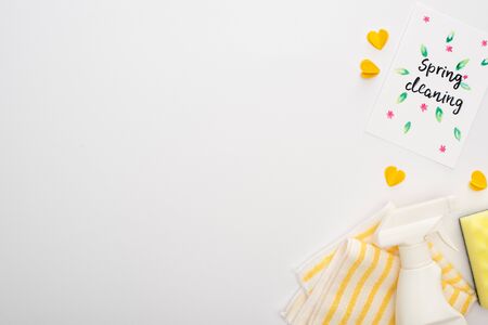 top view of yellow cleaning supplies and hearts near spring cleaning card on white background