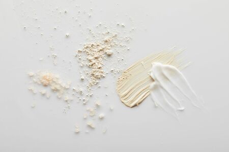 Top view of sea salt, face powder, cosmetic and tone cream brushstrokes on grey background