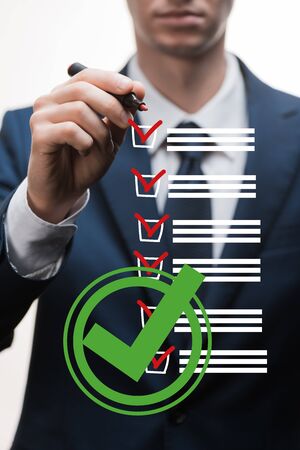 selective focus of businessman in formal wear holding marker pen near checklist on white, quality conceptの写真素材
