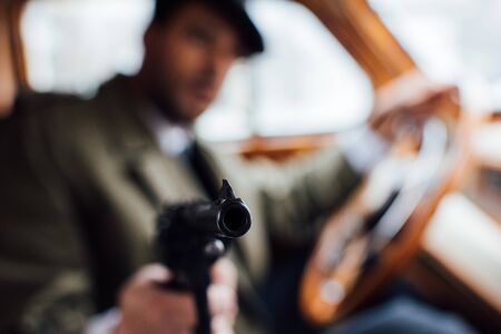 Selective focus of mafioso aiming gun while driving retro carの写真素材