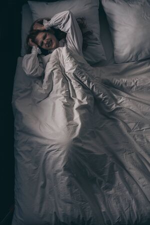 top view of paranormal girl in nightgown with headache lying in bed