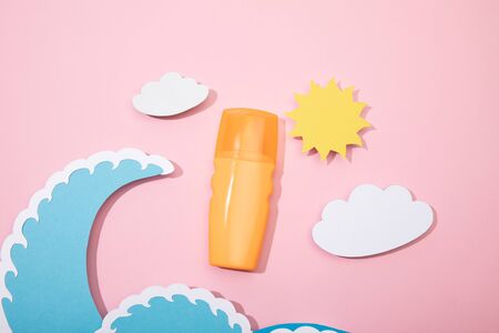 Top view of paper cut beach with dispenser bottle of sunscreen on pink background