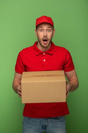 shocked delivery man in red uniform holding parcel on greenの写真素材