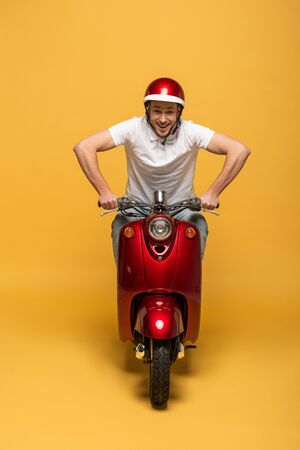 happy delivery man in helmet riding scooter on yellow backgroundの写真素材