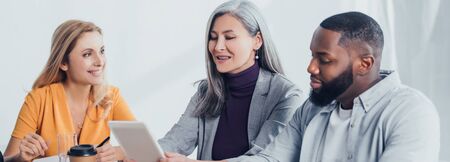 panoramic shot of smiling multicultural colleagues using digital tablet