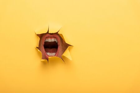 cropped view of open mouth in yellow paper holeの写真素材