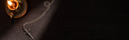 top view of burning candle and cross on dark background with sunlight, panoramic shot