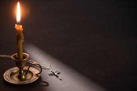 church candle in candlestick burning near catholic cross in dark with sunlight