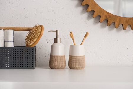 Box with hairbrush and towels near liquid soap and toothbrush holder with toothbrushes in bathroom,...