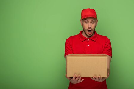 shocked delivery man in red uniform holding parcel on greenの写真素材