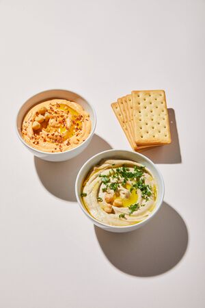 Bowls with delicious hummus and crackers on grey background