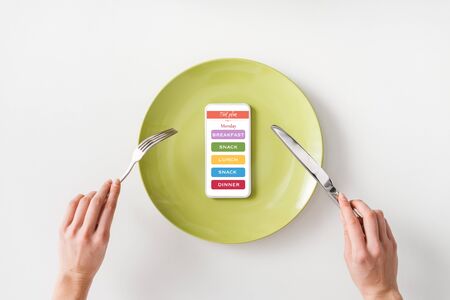 Top view of woman holding cutlery near smartphone on green plate on white backgroundの写真素材