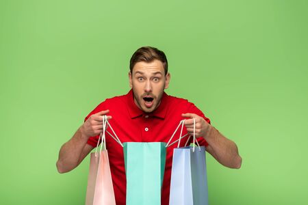 shocked young man holding shopping bags isolated on greenの写真素材
