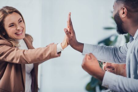 cropped view of smiling multicultural colleagues giving high five in creative agency
