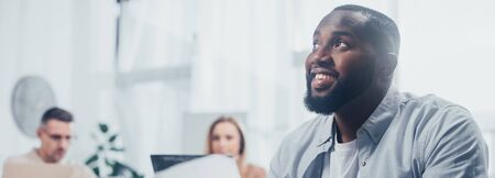 panoramic shot of smiling african american and colleagues on background