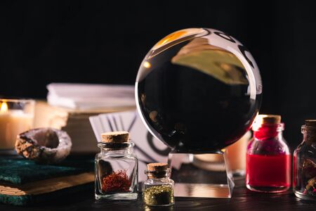 Selective focus of crystal ball with jars of dried herbs and tincture isolated on blackの写真素材