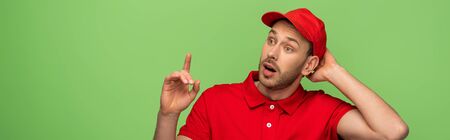 excited delivery man in red uniform showing idea gesture isolated on green, panoramic shotの写真素材