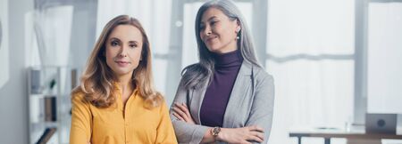 panoramic shot of smiling asian businesswoman with crossed arms looking at her colleagueの写真素材