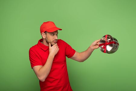 pensive delivery man in red uniform holding pan with bow on greenの写真素材