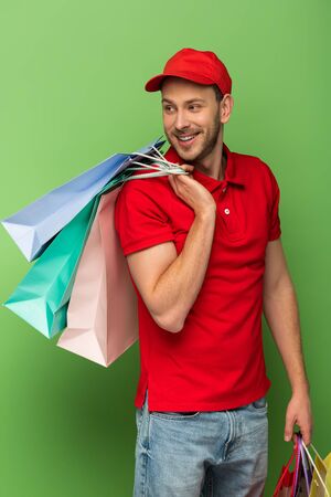 happy delivery man in red uniform holding shopping bags on green