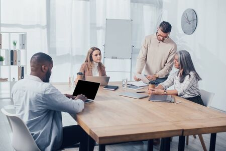 multicultural colleagues doing paper work and african american man using laptop