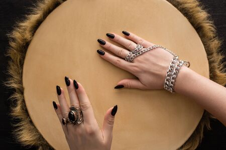 Top view of shaman with jewelry rings and chain on hands playing on tambourine isolated on black
