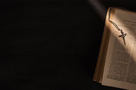 top view of open holy bible with cross on dark background with sunlight