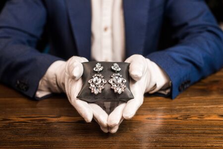 Cropped view of jewelry appraiser holding jewelry pillow with earrings at table isolated on blackの写真素材