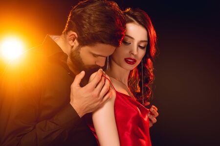 Side view of handsome man taking off dress from beautiful woman on black background with lighting