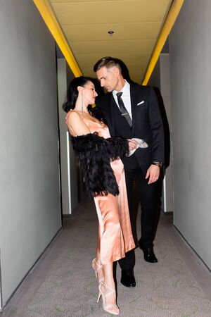 handsome boyfriend kissing smiling girlfriend in dress in hotel