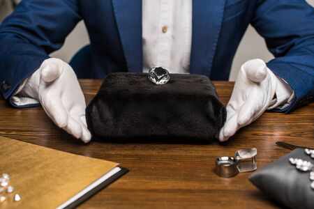 Cropped view of jewelry appraiser near gemstone and magnifying glass on tableの写真素材