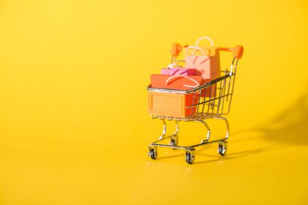 small shopping bags in toy shopping cart on yellowの写真素材