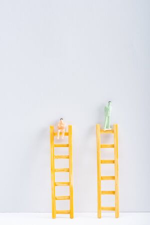 Two people figures on ladders on white surface on grey background with copy space, concept of equality rightsの写真素材