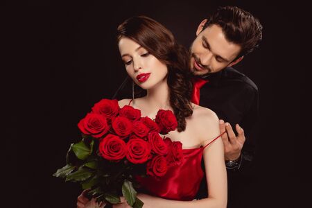 Elegant man taking off dress from girlfriend with red roses isolated on black