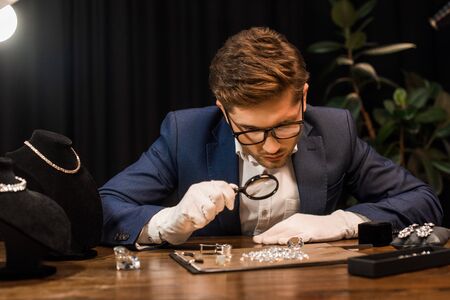 Handsome jewelry appraiser examining gemstones on board with magnifying glass on tableの写真素材