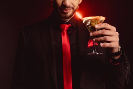 Cropped view of elegant man holding glass of cocktail on black background with lightingの写真素材