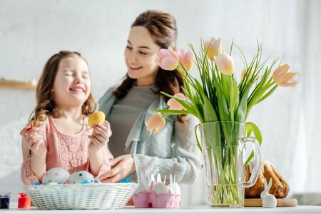 selective focus of tulips near chicken eggs, easter bread, happy mother and daughter