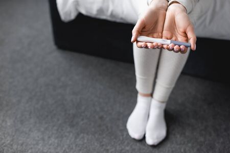 cropped view of woman sitting on bed and holding pregnancy test with negative resultの写真素材