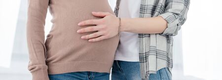 Cropped view of woman touching belly of pregnant girlfriend, panoramic shotの写真素材