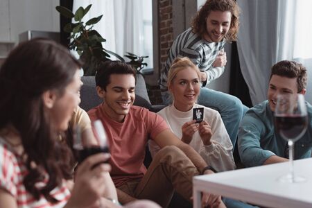 KYIV, UKRAINE - JANUARY 27, 2020: selective focus of smiling girl holding card while playing mafia game with friendsの写真素材