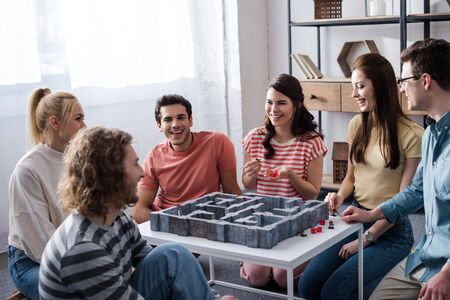 KYIV, UKRAINE - JANUARY 27, 2020: young smiling friends playing labyrinth game at home