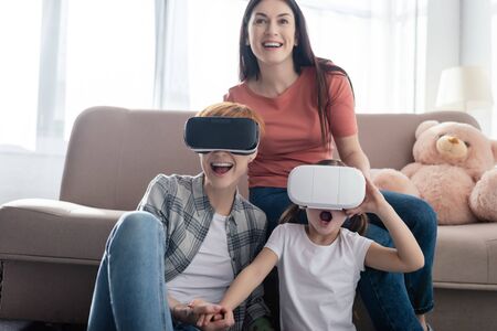 Shocked kid in vr headset holding hand of mother near parent at home