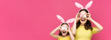 panoramic shot of excited mother and daughter in bunny ears covering eyes with easter eggs isolated...