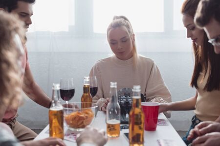 KYIV, UKRAINE - JANUARY 27, 2020: cheerful friends playing lotto game while sitting at table with drinks and chipsの写真素材